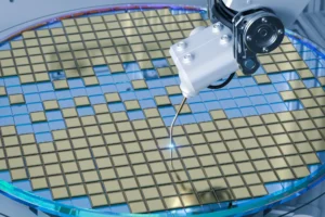 Illustration of a robotic tool working on a silicon wafer covered with a grid of gold-coloured dies, with a small bright spot at the tool tip, representing electronic fume extraction for the semiconductor industry