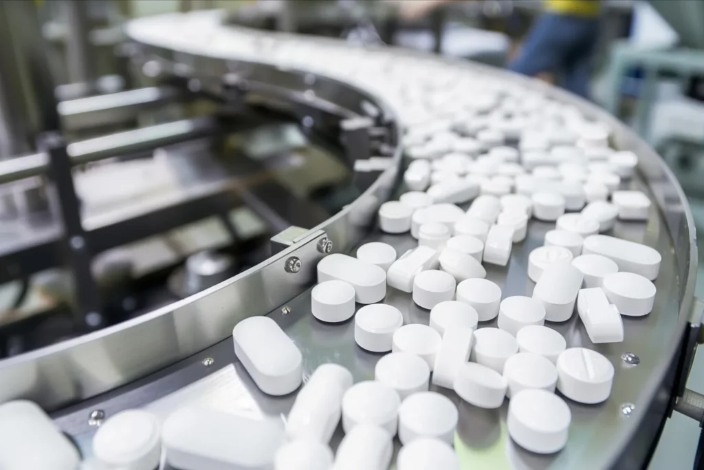 White tablets moving along a curved stainless-steel conveyor on a pharmaceutical production line, representing pharmaceutical applications for dust fume extractor solutions