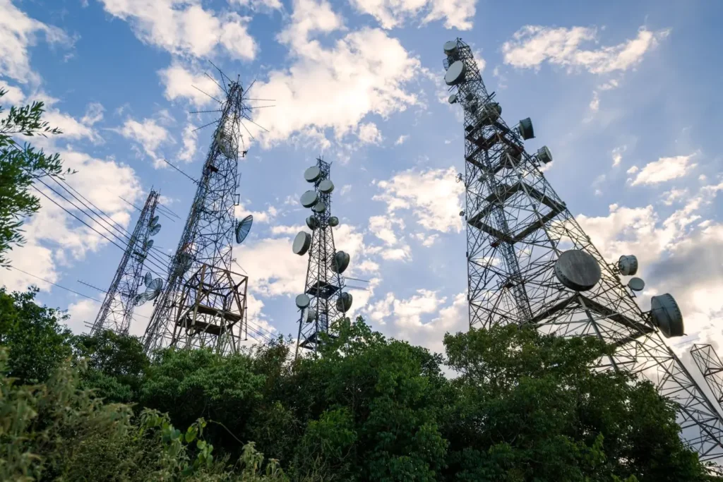 Lattice telecommunication towers with microwave dish antennas rising above trees against a blue sky, representing telecommunications and optical networks applications for the narrow linewidth tunable laser