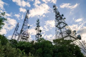Lattice telecommunication towers with microwave dish antennas rising above trees against a blue sky, representing telecommunications and optical networks applications for the narrow linewidth tunable laser